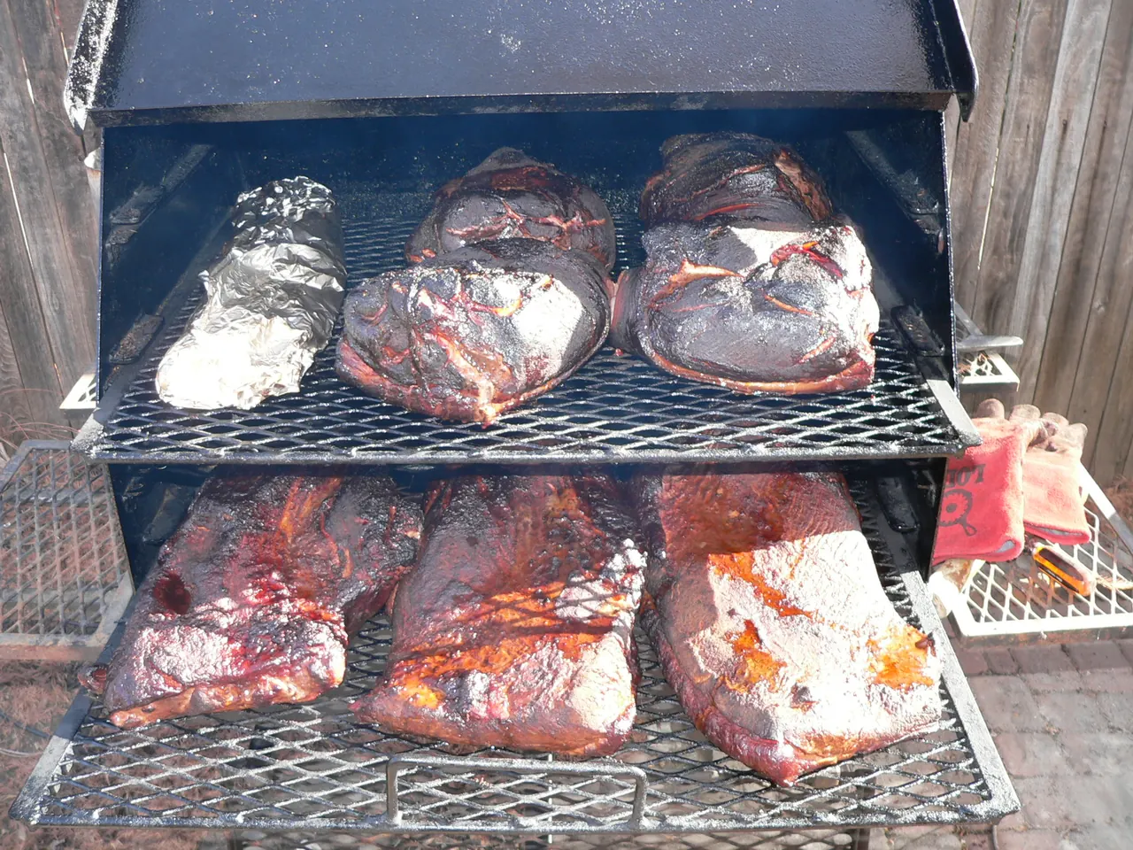Several briskets, pork shoulders, and a rib rack prepared for a long smoke