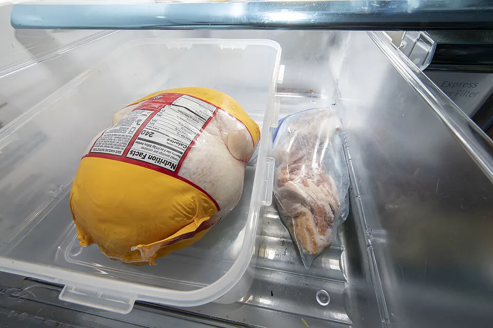 Wrapped poultry and another food package set inside clear trays on a refrigerator shelf